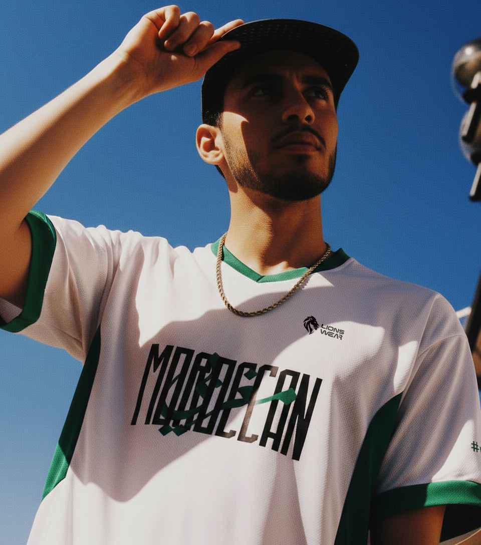Close-up of a Moroccan supporter wearing the Lions Wear Moroccan AURA white and green jersey under bright sky — CAN 2025 apparel.