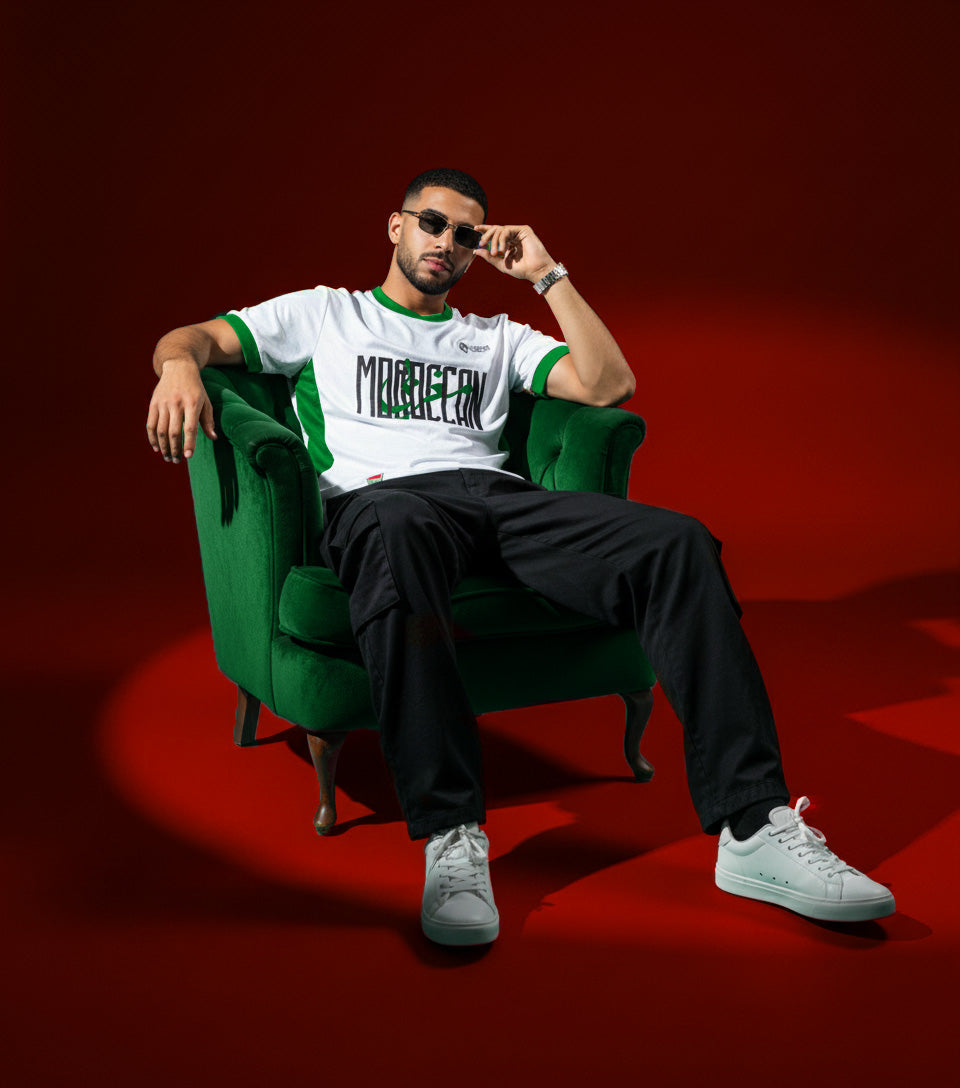 Moroccan supporter wearing the Lions Wear Moroccan AURA jersey, sitting confidently on a green chair in a red studio — premium CAN 2025 fashion style.