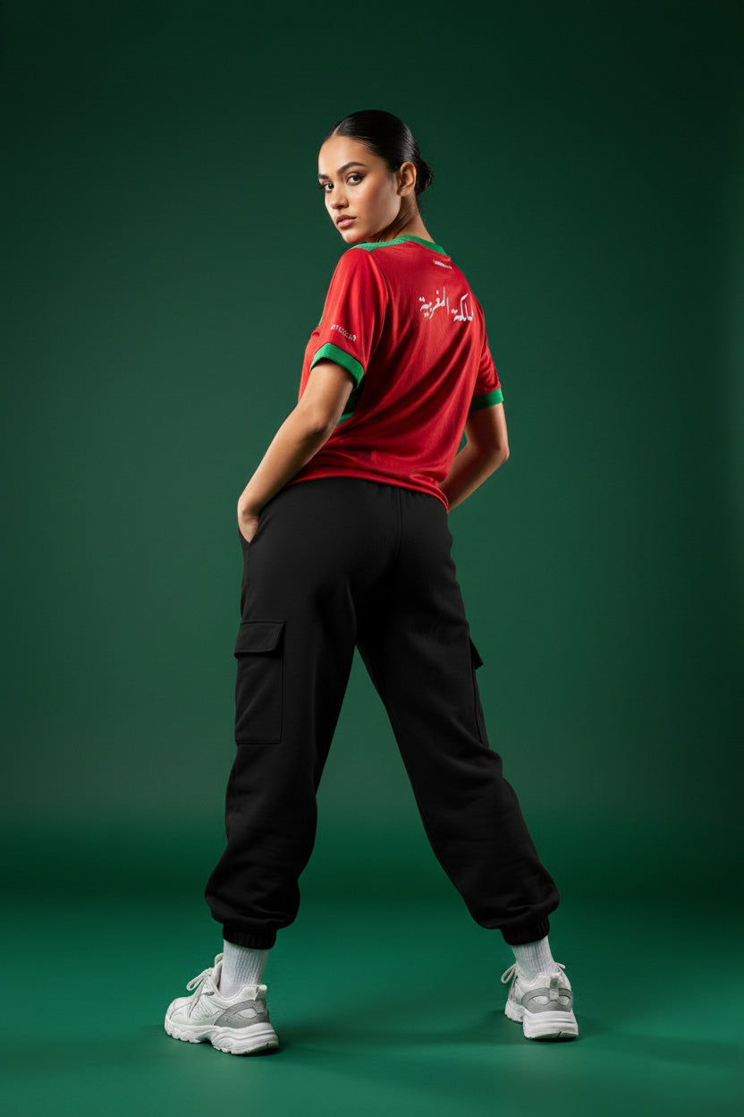 Back view of a young Moroccan woman wearing the Lions Wear Red Flow #morocCAN jersey with Arabic ‘Kingdom of Morocco’ design — supporter apparel for CAN 2025.