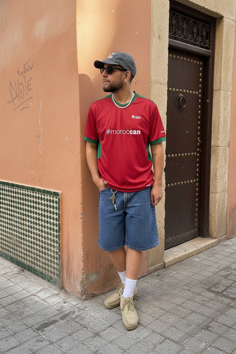 Moroccan man wearing the Lions Wear Red Flow jersey with #morocCAN design, casual street style near a traditional Moroccan door.